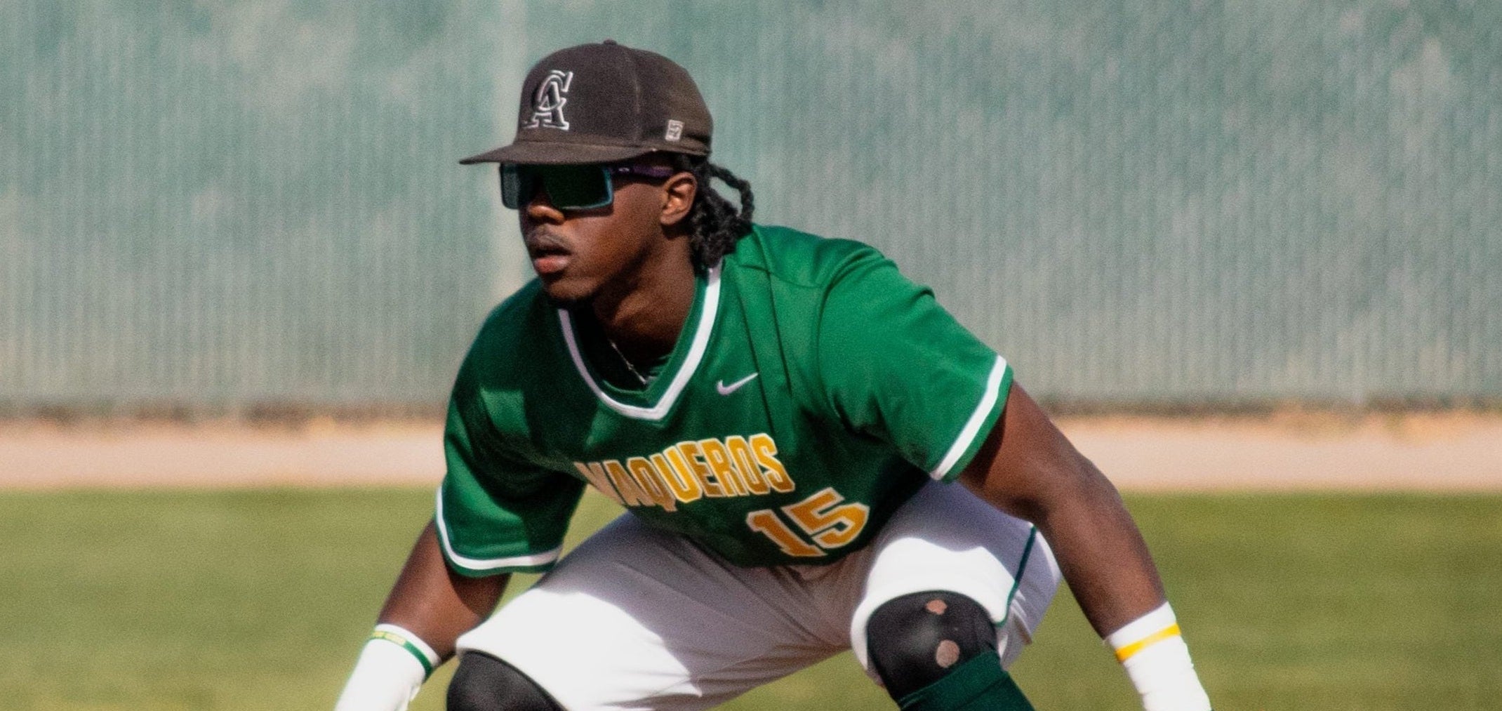 Baseball player in green uniform with sunglasses and protective gear on a field