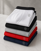 Stack of folded pants in black, white, gray, red, and navy on a light surface with a neutral background.