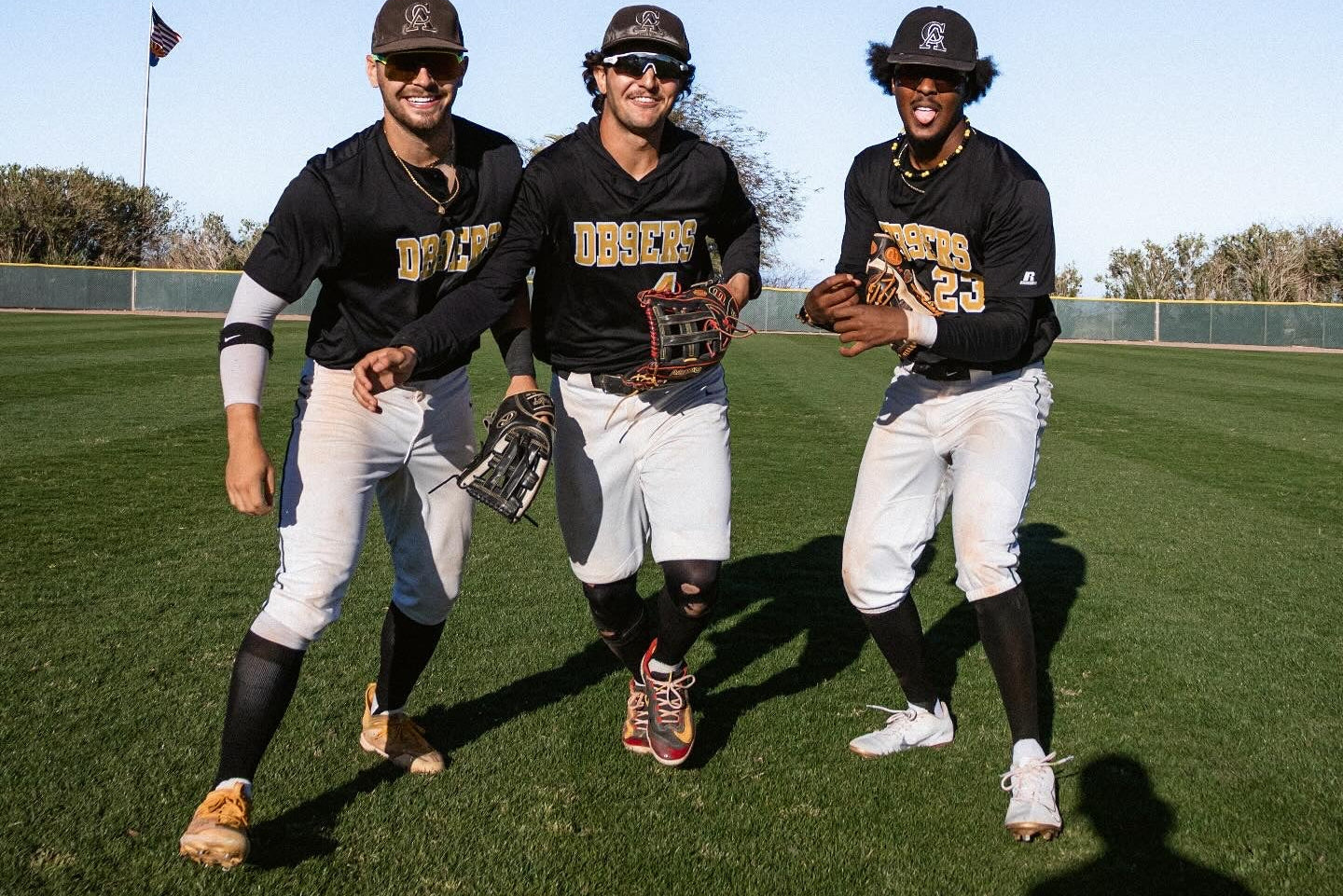 Three baseball players in uniforms on a field with clear blue sky
