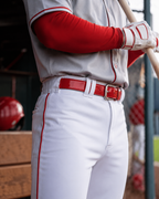 Baseball player in red and white uniform holding a bat in a dugout.