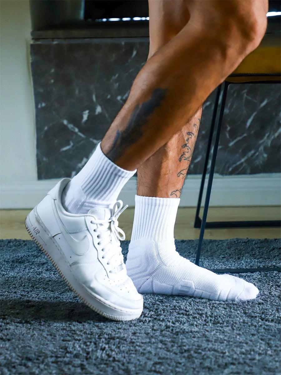 Person wearing white sneakers and socks on a textured floor.