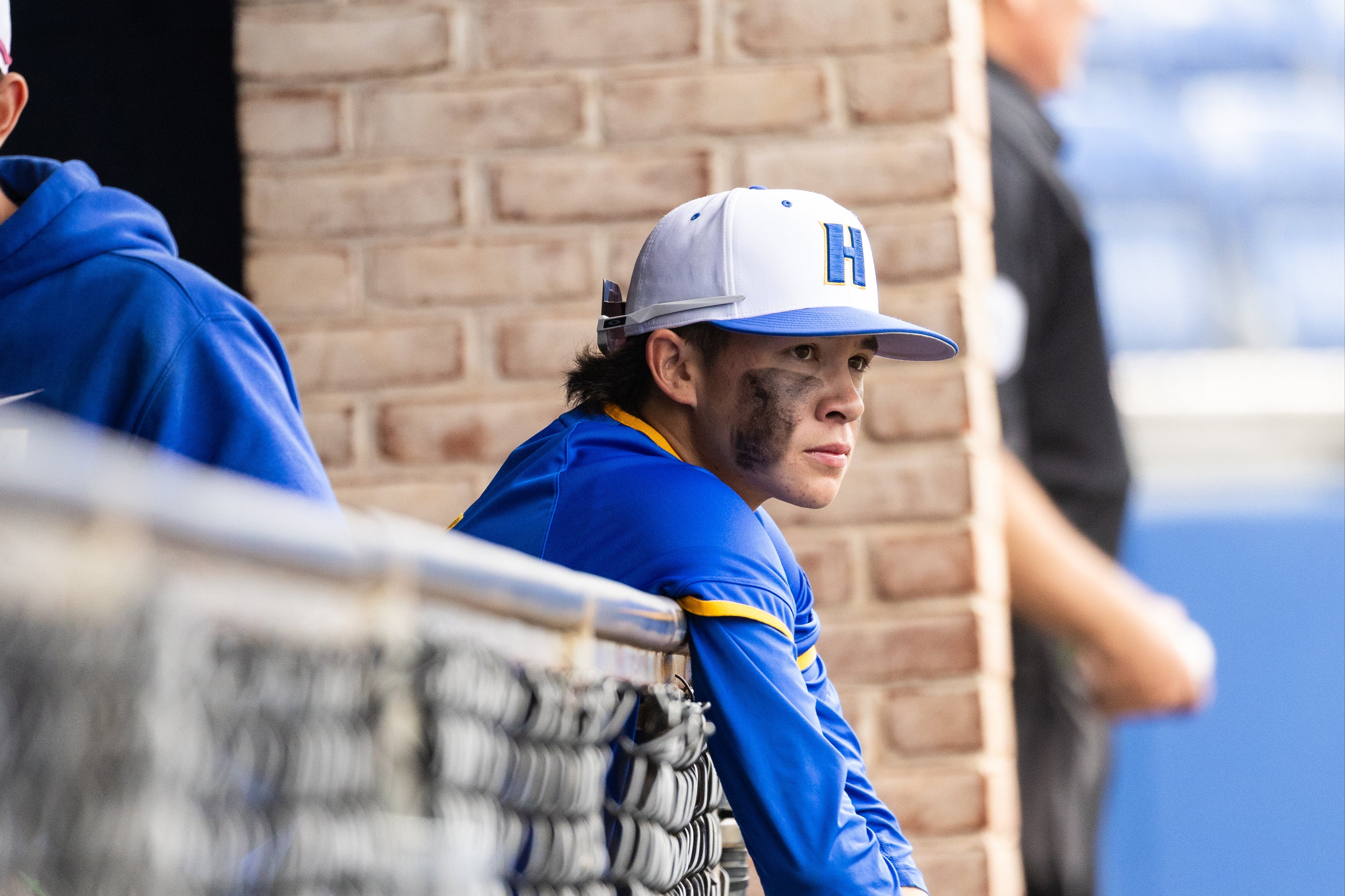 Person in blue uniform leaning on a railing, looking off to the side.