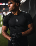 Athlete wearing a black t-shirt with a logo and gloves on a sports field.
