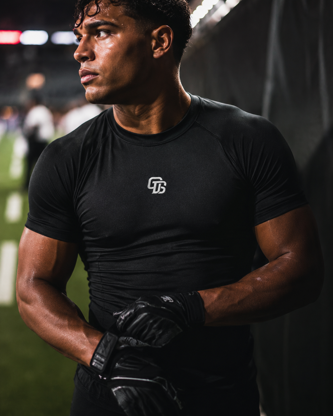 Athlete wearing a black t-shirt with a logo and gloves on a sports field.