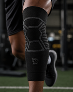 Person wearing a black knee brace with a logo on a sports field.