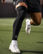 Person running on a grassy field wearing black compression leg sleeves with a logo.