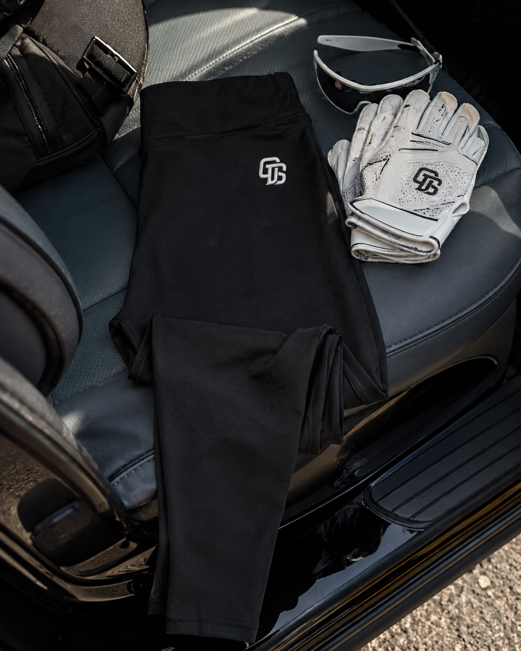 Black pants with a logo, white gloves, and sunglasses on a car seat