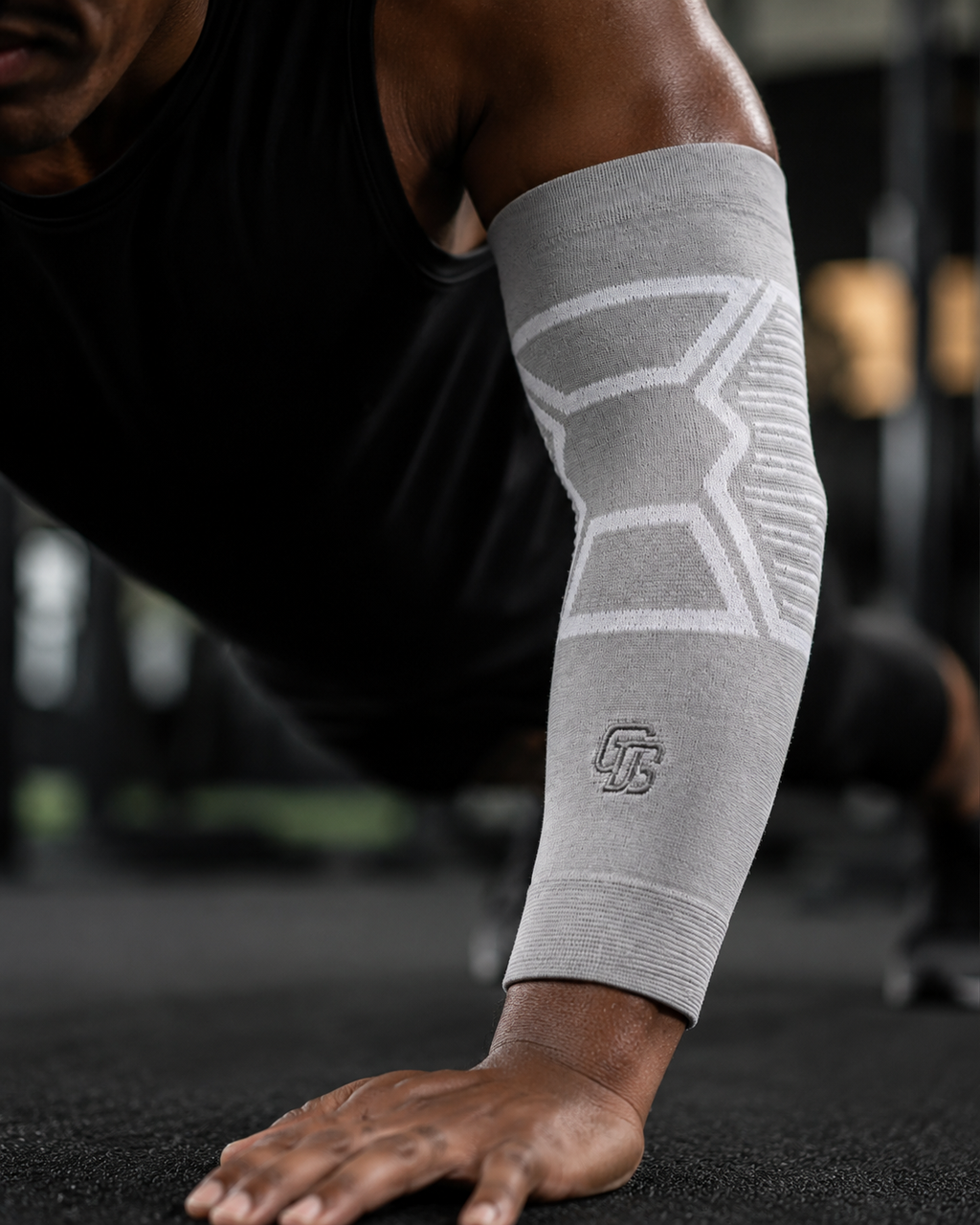 Person wearing a gray compression sleeve on their arm with a blurred gym background