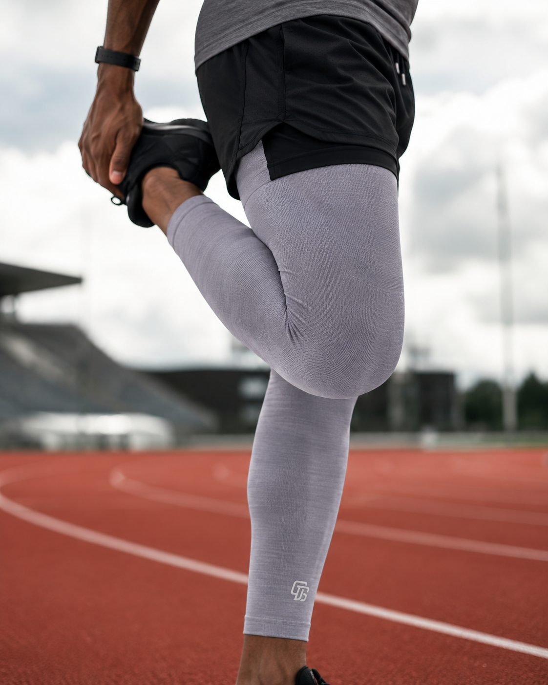 Person stretching on a running track wearing gray leggings with a logo.