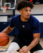 Basketball player holding a ball on a court with a visible logo on his shirt.