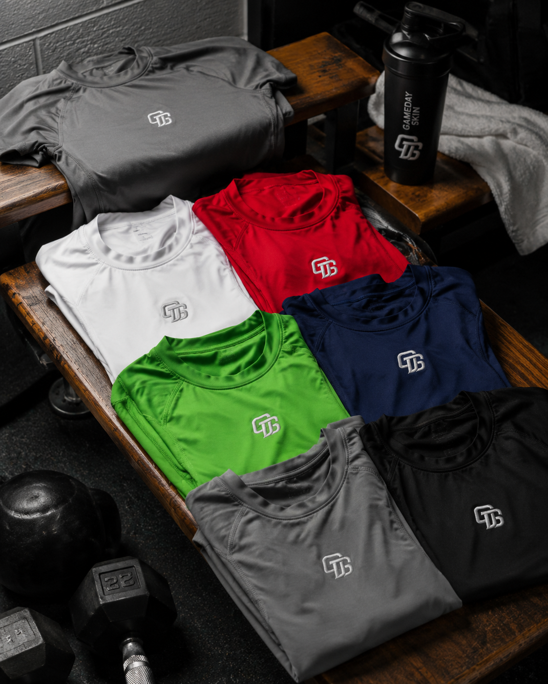 Folded athletic wear with logos on a wooden surface, including shirts and shorts in various colors.