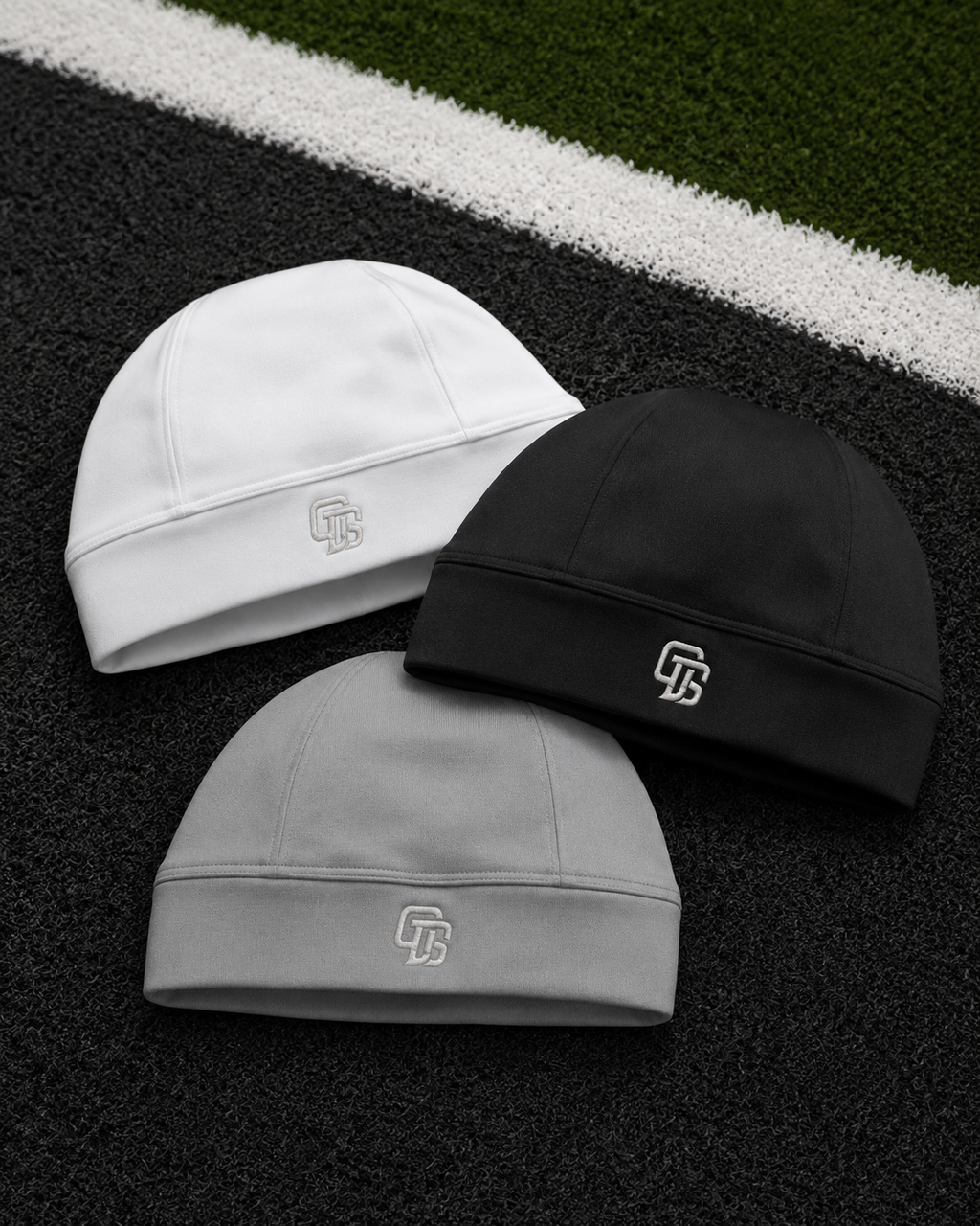 Three beanies in white, black, and gray on a sports field background.