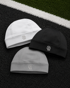 Three beanies in white, black, and gray on a sports field background.