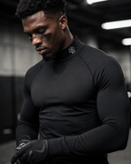 Person wearing a black long-sleeve athletic shirt with a logo, standing indoors.